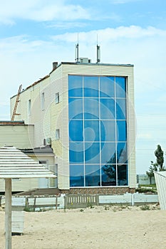 Beautiful apartments with glass windows, modern architecture house by the sea, sandy beach, blue cloudy sky.