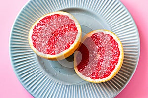 Beautiful appetizer fresh red grapefruit citrus fruit with half slice on blue plate and pink background close up top view natural