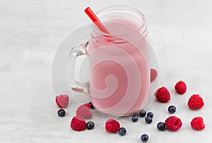 Beautiful appetizer pink raspberries and blueberry fruit smoothie or milkshake in glass jar with berries background. Yogurt