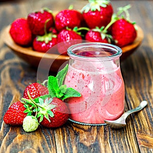 Beautiful appetizer red strawberry fruit smoothie or milk shake in glass jar with berries on wooden background, top view. Yogurt c
