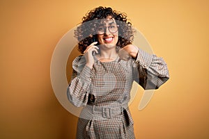 Beautiful arab businesswoman wearing glasses having conversation talking on smartphone with surprise face pointing finger to