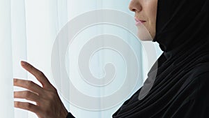Beautiful arab woman in hijab waiting for husband, looking in window, close-up