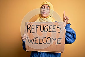 Beautiful arab woman wearing islamic hijab holding banner with refugees welcome message surprised with an idea or question