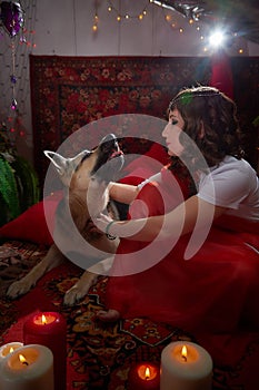 Beautiful arabian girl with candles and big dog in red room full of rich fabrics and carpets in sultan harem. Photo