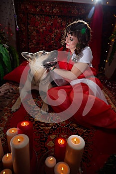 Beautiful arabian girl with candles and big dog in red room full of rich fabrics and carpets in sultan harem. Photo
