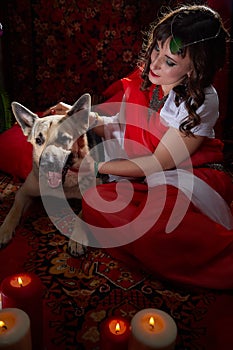 Beautiful arabian girl with candles and big dog in red room full of rich fabrics and carpets in sultan harem. Photo