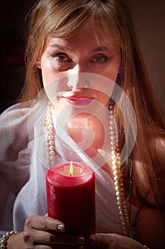 Beautiful arabian girl with candles in red room full of rich fabrics and carpets in sultan harem. Photo shoot of woman