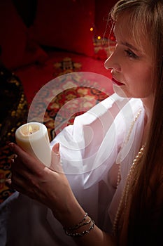 Beautiful arabian girl with candles in red room full of rich fabrics and carpets in sultan harem. Photo shoot of woman