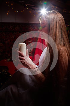 Beautiful arabian girl with candles in red room full of rich fabrics and carpets in sultan harem. Photo shoot of woman