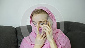 Beautiful arabian woman in pink hijab sitting on a sofa in a cafe and talking on cell phone