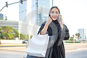 Beautiful Arabic woman carrying shopping bags and talking on mobile phone on a city street.