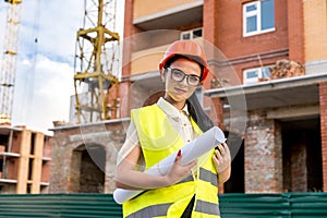 Beautiful architect with blueprints in rolls on construction site