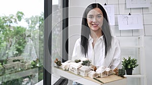 Beautiful architect shows house model while standing with confident. Immaculate.