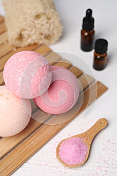 Beautiful aromatic bath bombs and sea salt on white wooden table, closeup