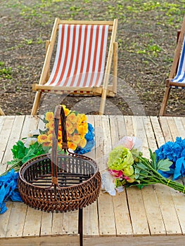 Beautiful artificial bouquets of various colors placed on wooden table among deck chairs in garden. Multi-colored artificial