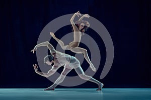 Beautiful, artistic, young couple, man and woman dancing ballet against blue studio background. Impressive art