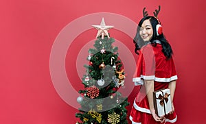 Beautiful asia woman in red santy costume holding gift box Isolated red background and christmas tree