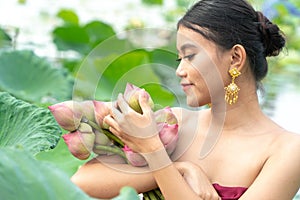 Beautiful asia women wearing traditional Thai dress and sitting on wooden boat in flower lotus lake. Her hands are holding a pink