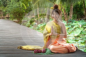 Beautiful asia women wearing traditional Thai dress and sitting on wooden bridge. Her hand is in the respect hands in thailand sty