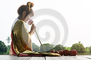 Beautiful asia women wearing traditional Thai dress and sitting on Wooden floor. Her hands is holding lotus flower and smell pink