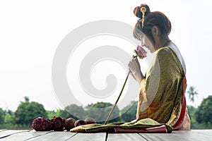 Beautiful asia women wearing traditional Thai dress and sitting on Wooden floor. Her hands is holding lotus flower and smell pink