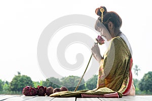 Beautiful asia women wearing traditional Thai dress and sitting on Wooden floor. Her hands is holding lotus flower and smell pink