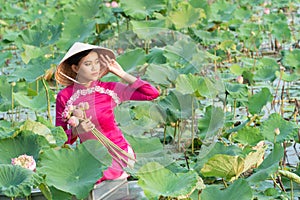 Beautiful asia women wearing white pink traditional Vietnam dress Ao Wai and Vietnam farmer`s hat and sitting on wooden boat in