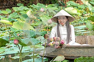 Beautiful asia women wearing white traditional Vietnam dress Ao Wai and Vietnam farmer`s hat and sitting on wooden boat in