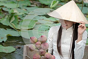 Beautiful asia women wearing white traditional Vietnam dress Ao Wai and Vietnam farmer`s hat and sitting on wooden boat in flow