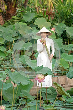 Beautiful asia women wearing white white traditional Vietnam dress Ao Wai and Vietnam farmer`s hat and standing on wooden boat