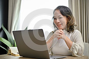 Beautiful Asian-aged businesswoman working in her home living room, using laptop. work from home