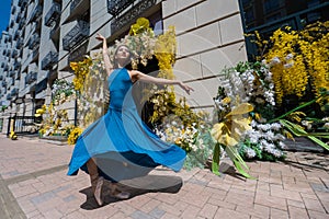 Beautiful Asian ballerina dances against the background of a building decorated with flowers.