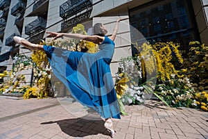 Beautiful Asian ballerina dances against the background of a building decorated with flowers.