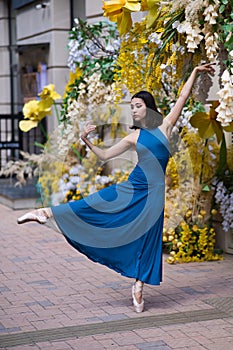 Beautiful Asian ballerina dances against the background of a building decorated with flowers. Vertical photo.