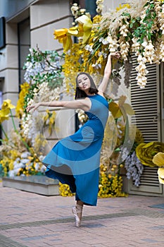 Beautiful Asian ballerina dances against the background of a building decorated with flowers. Vertical photo.
