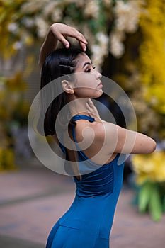 Beautiful Asian ballerina posing against the backdrop of a building decorated with flowers.