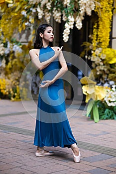 Beautiful Asian ballerina posing against the backdrop of a building decorated with flowers.