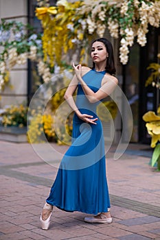 Beautiful Asian ballerina posing against the backdrop of a building decorated with flowers.