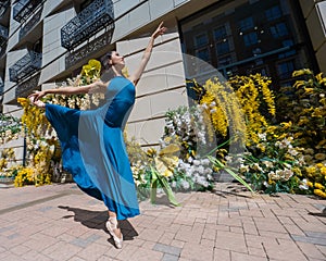 Beautiful Asian ballerina posing against the backdrop of a building decorated with flowers.