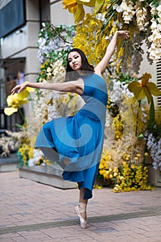 Beautiful Asian ballerina posing against the backdrop of a building decorated with flowers.