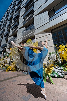 Beautiful Asian ballerina posing against the backdrop of a building decorated with flowers.