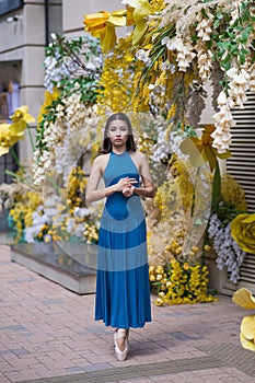 Beautiful Asian ballerina posing against the backdrop of a building decorated with flowers.