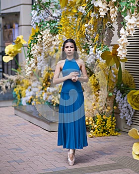 Beautiful Asian ballerina posing against the backdrop of a building decorated with flowers.