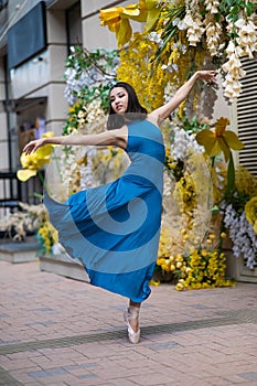 Beautiful Asian ballerina posing against the backdrop of a building decorated with flowers.