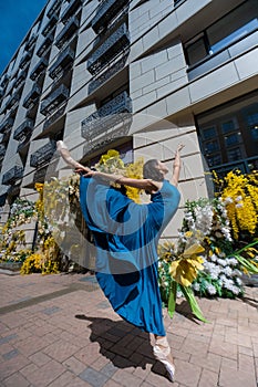 Beautiful Asian ballerina posing against the backdrop of a building decorated with flowers.