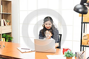Beautiful Asian business mom is using a laptop  while spending time with her cute baby boy at home for quarantine from virus