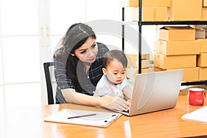Beautiful Asian business mom is using a laptop  while spending time with her cute baby boy at home for quarantine from virus