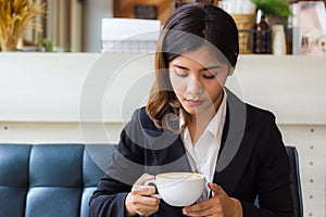 A beautiful asian business woman sitting on sofa and looking cup of hot coffee in her hand.