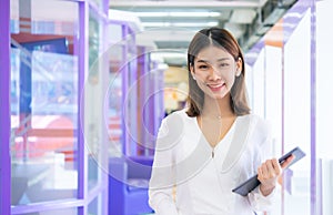 Beautiful asian business woman is standing facing the camera confidently holding a tablet with one hand and smiling.