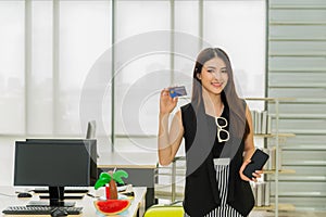 Beautiful asian business woman standing smiling holding credit card and mobile phone